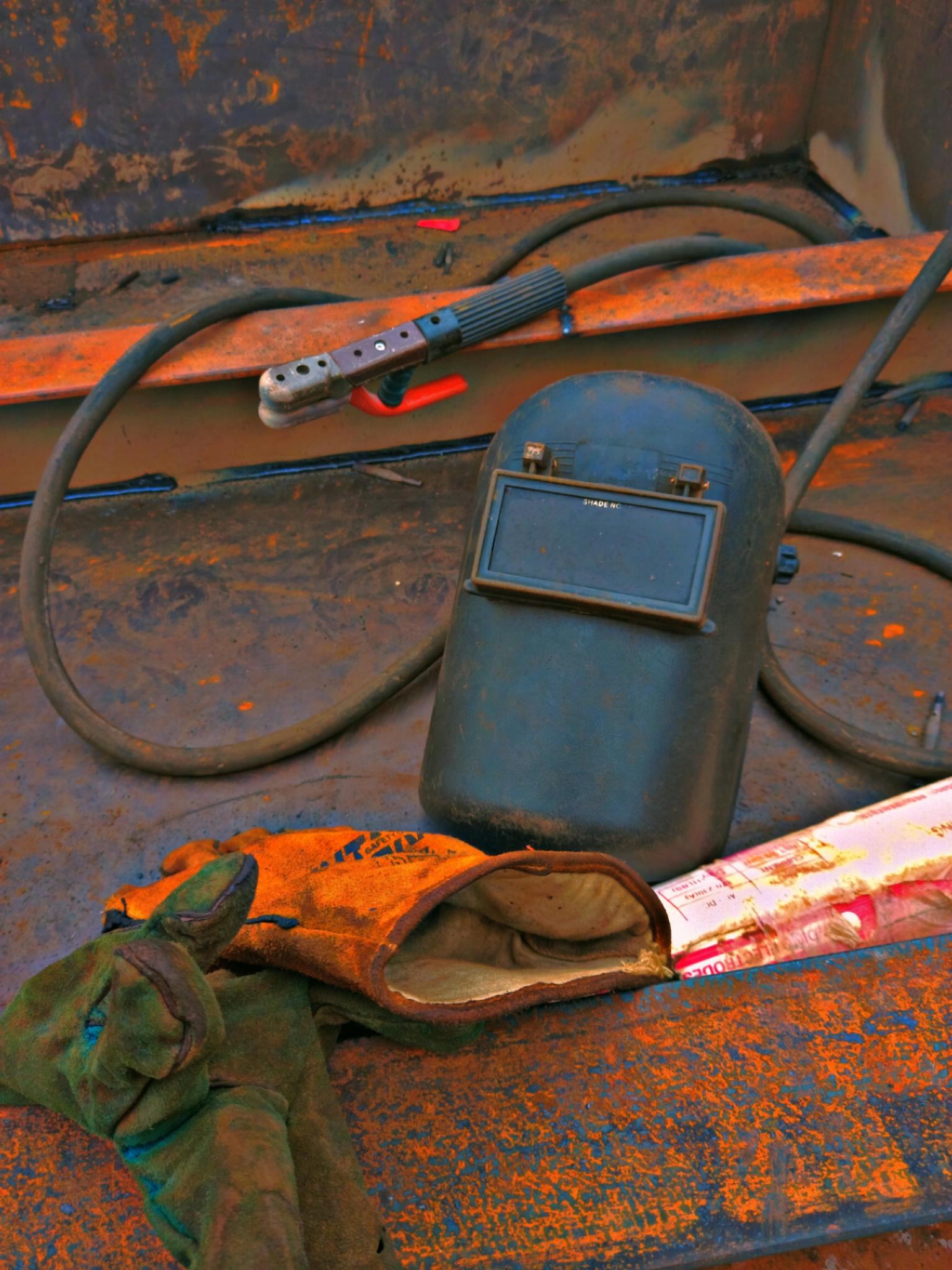 Close-up of a welding helmet and gloves on rusty metal, highlighting safety and industry.